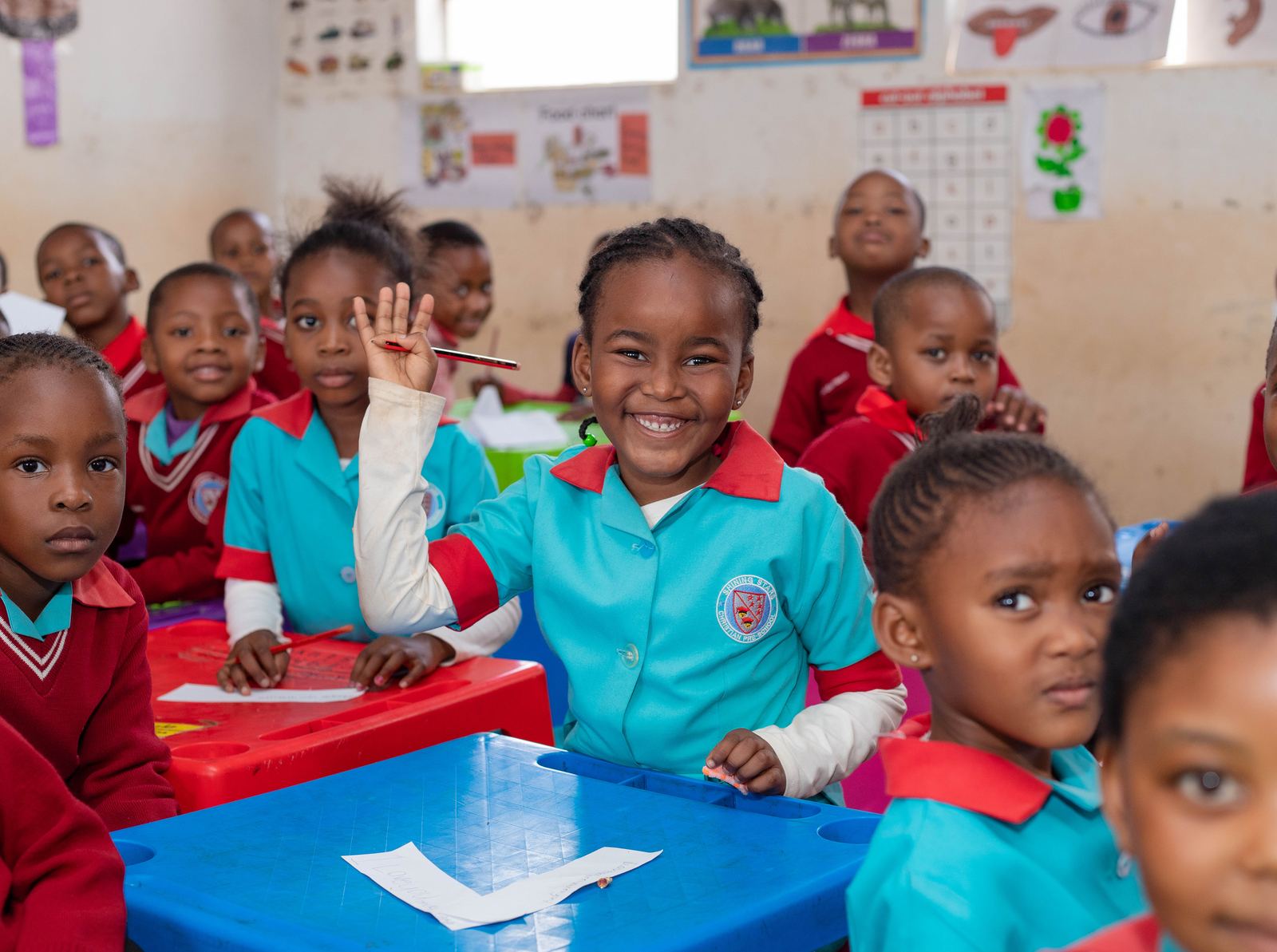 A Shining Stars pupil smiling and raising her hand in class